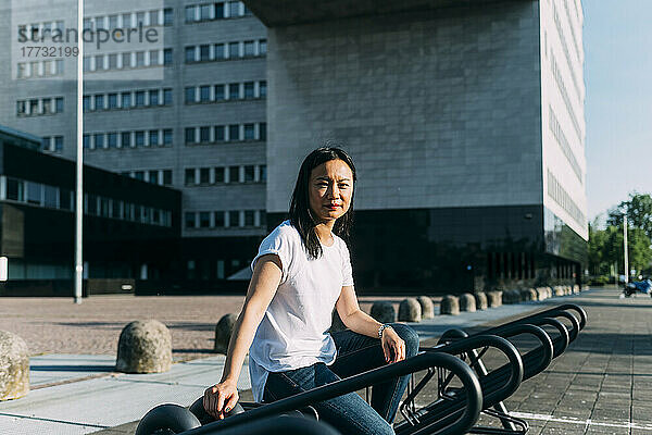 Geschäftsfrau sitzt an sonnigem Tag auf Fahrradständer