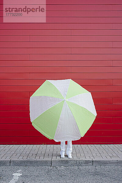 Woman hiding behind umbrella in front of red wall