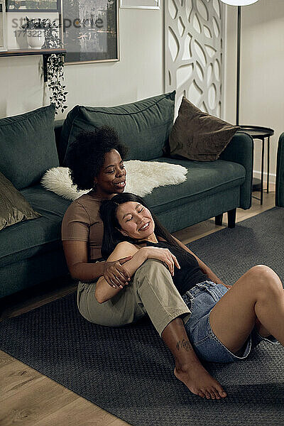 Lesbians sitting together in front of sofa at home