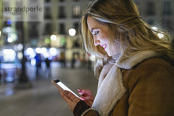 Lächelnde Frau  die nachts ihr Smartphone benutzt