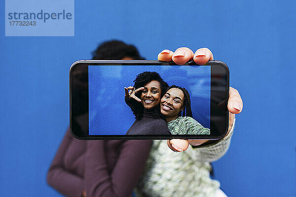 Fröhliche Freunde machen Selfies mit dem Smartphone vor der blauen Wand