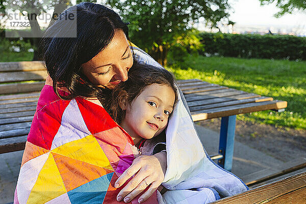 Mutter und Tochter im Park in eine Steppdecke gehüllt