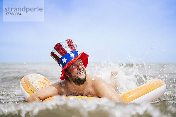 Sorgloser Mann mit Uncle-Sam-Hut schwimmt mit Poolfloß im Meer