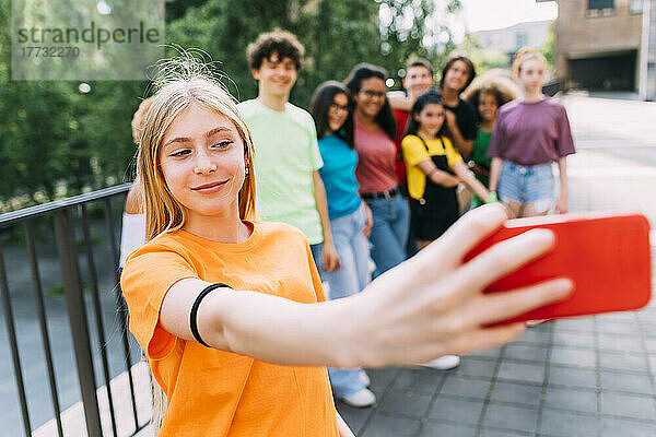 Smiling blond girl taking selfie through mobile phone with friends