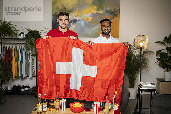 Happy football fans standing with Swiss flag at home