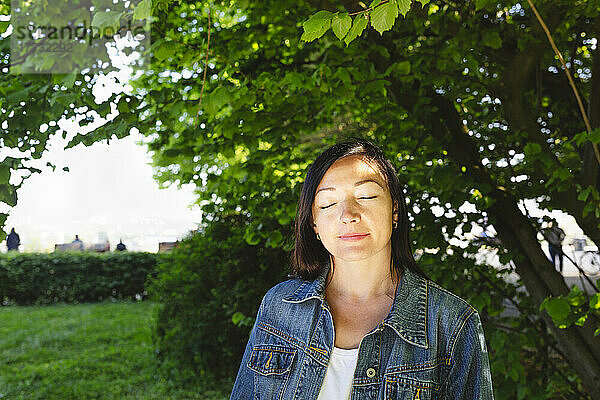Frau trägt Jeansjacke mit geschlossenen Augen im Park