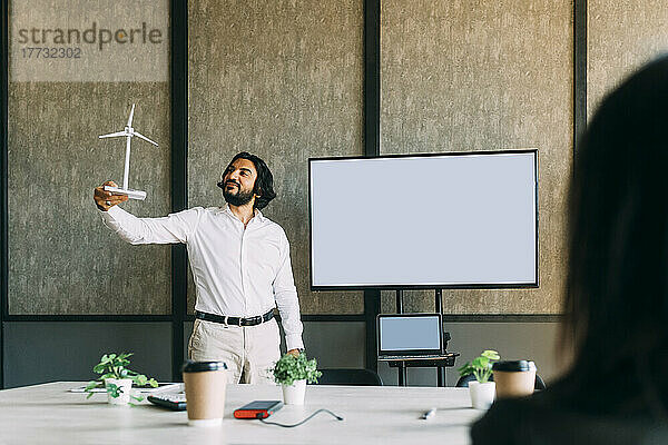 Businessman with wind turbine model giving presentation to colleague at office