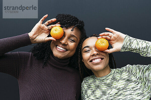 Fröhliche Freunde bedecken ihr Auge mit Orange vor der Wand