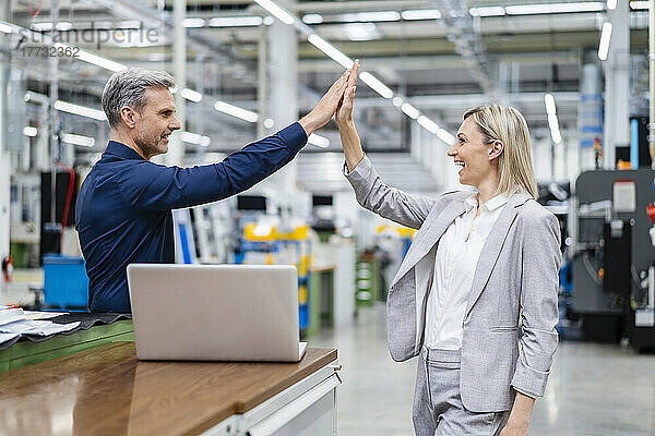 Glücklicher Geschäftsmann und Geschäftsfrau beim High Five in der Fabrik