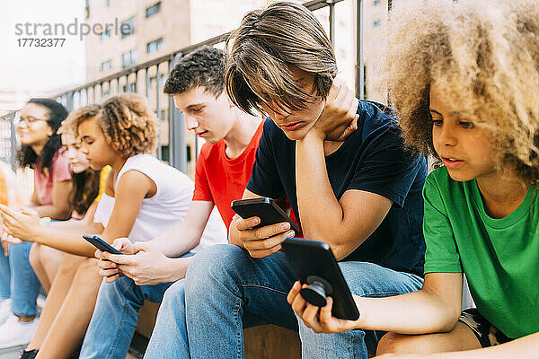Freunde benutzen Mobiltelefone und sitzen am Geländer
