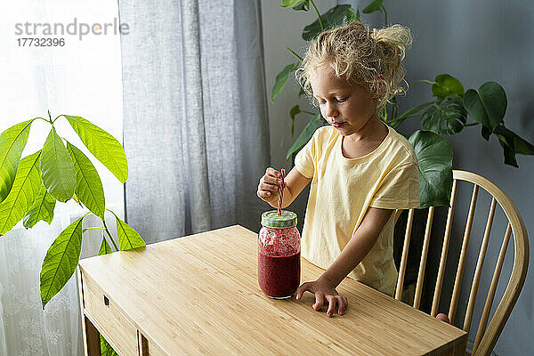 Mädchen mischt Erdbeer-Smoothie-Saft durch Strohhalm