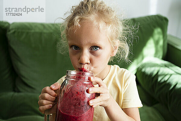 Mädchen trinkt Smoothie und sitzt zu Hause auf dem Sofa