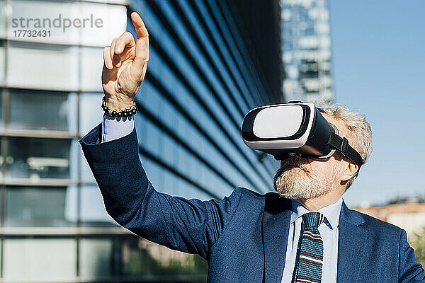Leitender Geschäftsmann mit Virtual-Reality-Headset gestikuliert vor Bürogebäude