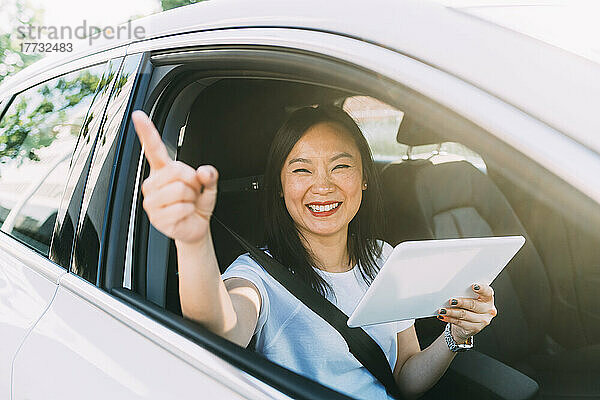 Glückliche Geschäftsfrau zeigt mit Tablet-PC im Auto auf Roadtrip