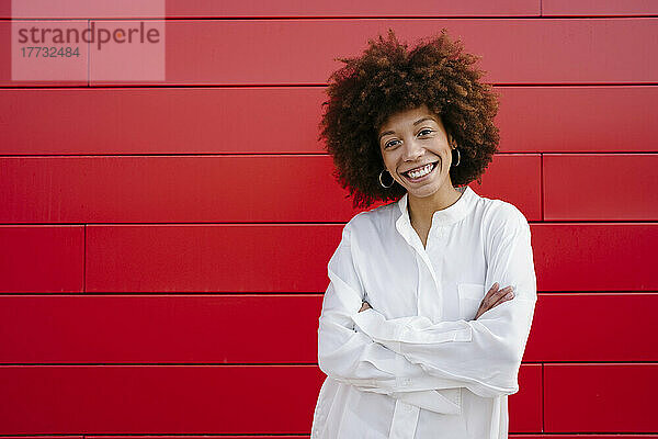 Lächelnde Afro-Frau steht mit verschränkten Armen vor einer roten Wand