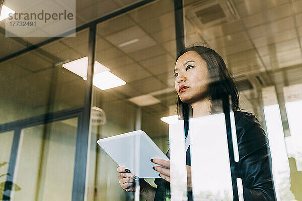 Selbstbewusste Geschäftsfrau mit Tablet-PC  gesehen durch Glas im Büro