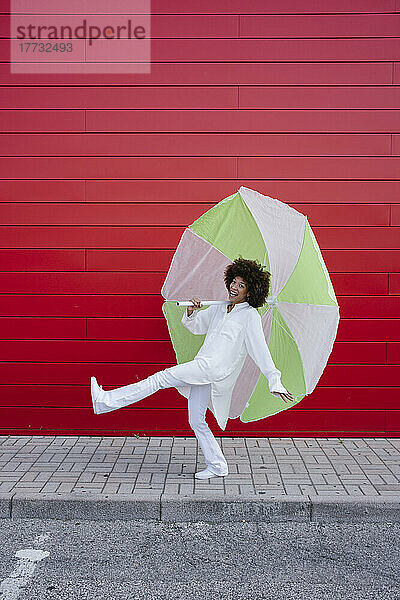 Fröhliche junge Frau mit Regenschirm geht auf Fußweg