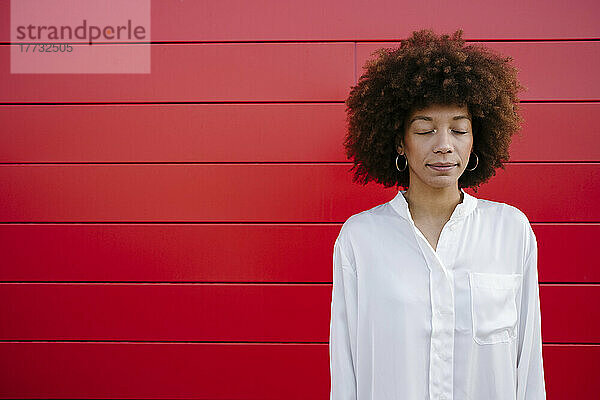 Afro-junge Frau mit geschlossenen Augen vor roter Wand