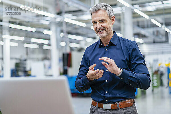 Mature businessman gesturing during video call on laptop in factory