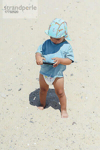 Junge mit Smartphone steht auf Sand am Strand