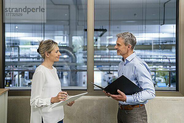 Geschäftsmann mit Klemmbrett und Geschäftsfrau mit digitalem Tablet unterhalten sich im Fabrikbüro