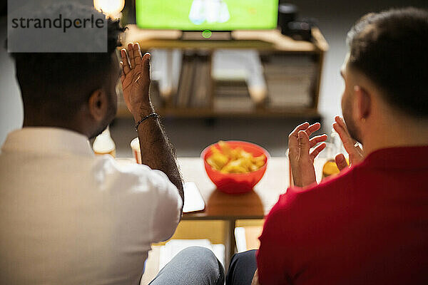 Junge Männer gestikulieren und schauen sich zu Hause ein Fußballspiel an