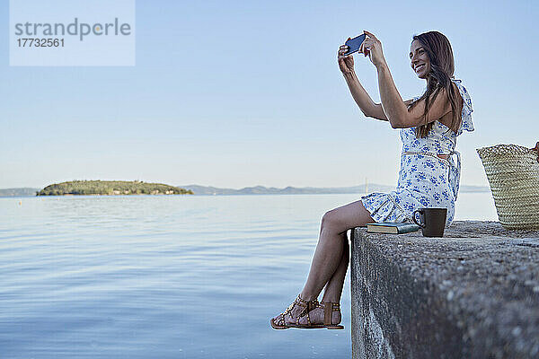 Lächelnde Frau fotografiert den See per Smartphone