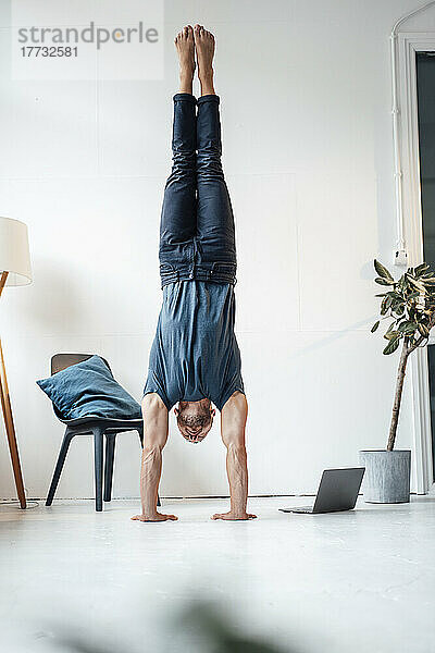 Mann macht zu Hause Handstand am Stuhl vor der Wand