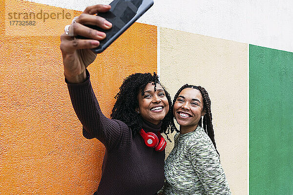 Fröhliche Freunde machen Selfies mit dem Smartphone vor der Wand