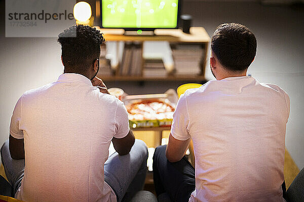 Young roommates watching football match together at home