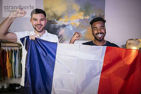 Fröhliche junge Männer mit französischer Flagge jubeln zu Hause