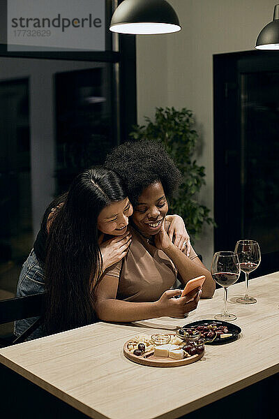 Glückliche Frau umarmt ihre Freundin und macht ein Selfie mit dem Smartphone  das am Tisch sitzt