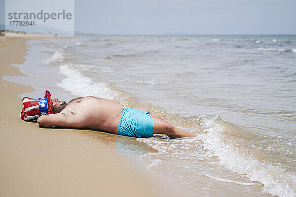 Sorgloser  hemdloser Mann mit Uncle Sam-Hut entspannt sich am Strand in der Nähe der Küste