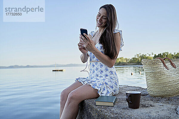 Glückliche Frau benutzt Mobiltelefon auf Steg am See