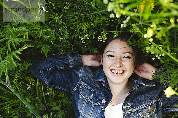 Cheerful teenage girl lying on grass in park