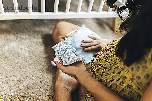 Schwangere Frau mit Babyschuhen sitzt zu Hause