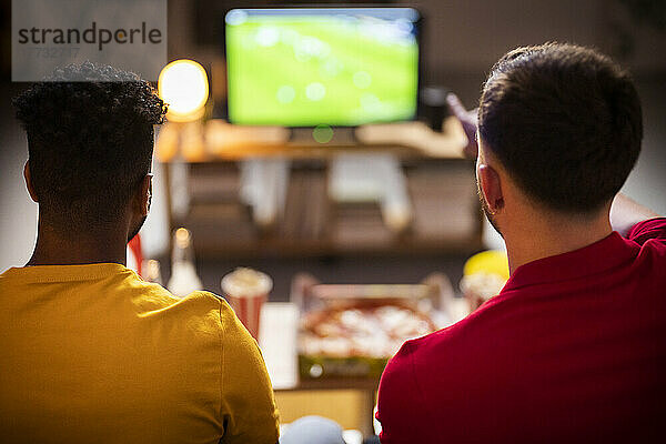 Young roommates watching soccer match at home