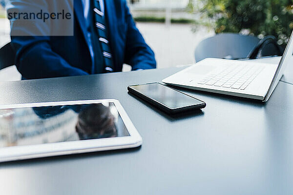 Geschäftsmann sitzt mit Tablet-PC  Smartphone und Laptop im Freien
