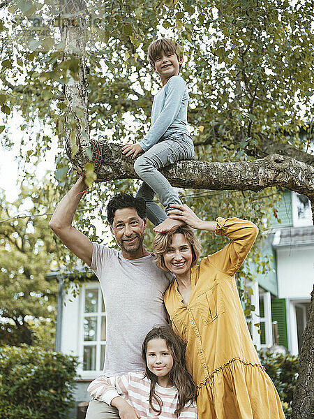 Glückliche Familie mit einem Jungen  der auf einem Baum im Hinterhof sitzt