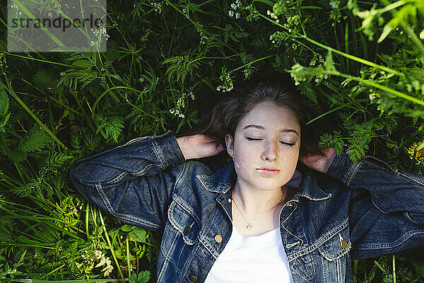 Girl in denim jacket relaxing with eyes closed on grass