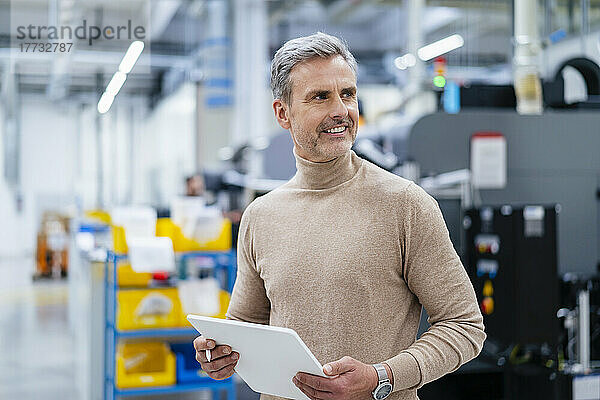 Smiling businessman holding digital tablet in factory