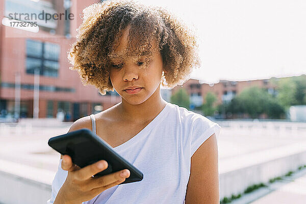 Afro-Frisur mit Smartphone an einem sonnigen Tag
