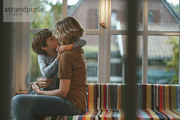 Zärtliche Mutter und Sohn küssen sich zu Hause auf dem Sofa