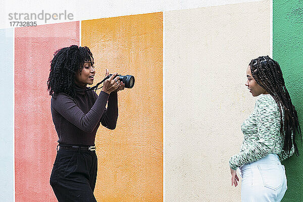 Frau fotografiert Freundin mit Kamera vor Wand