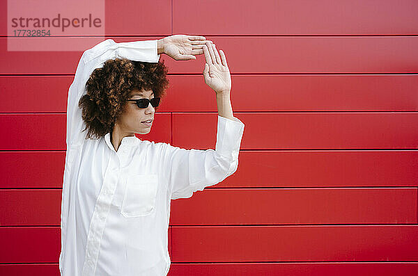 Afro-Frau mit Sonnenbrille macht Handzeichen vor roter Wand