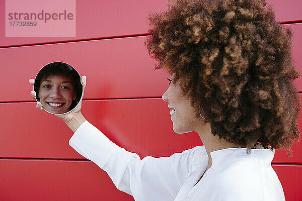 Spiegelung des Gesichts einer Frau auf einem runden Spiegel an einer roten Wand