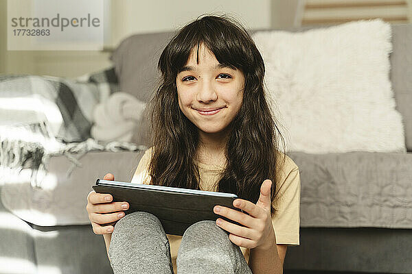 Lächelndes Mädchen mit Tablet-PC im Wohnzimmer