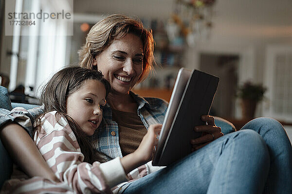 Glückliche Frau sitzt mit ihrer Tochter und benutzt zu Hause einen Tablet-PC