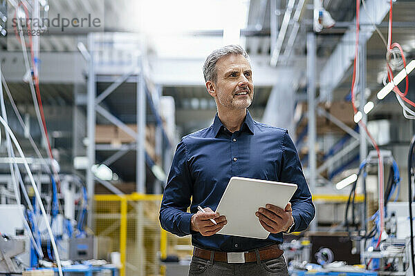 Reifer Geschäftsmann hält digitales Tablet in der Fabrik