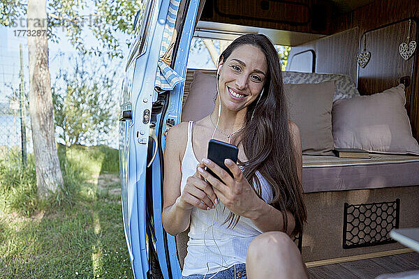 Lächelnde Frau mit Smartphone  die im Wohnmobil Musik über In-Ear-Kopfhörer hört